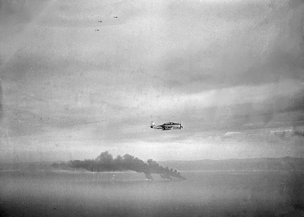 A U.S. Navy Grumman TBM-3 Avenger of torpedo squadron VT-11 from the aircraft USS Hornet (CV-12) flies past three Japanese oilers burning in Cam Ranh Bay, Indochina (later Vietnam), on 12 January 1945.